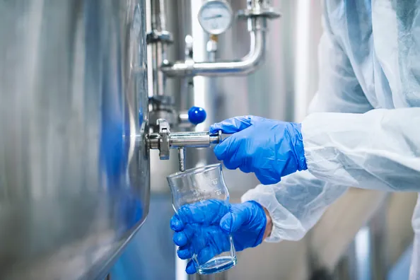 Técnico con guantes tomando una muestra de agua de un tanque industrial de acero inoxidable
